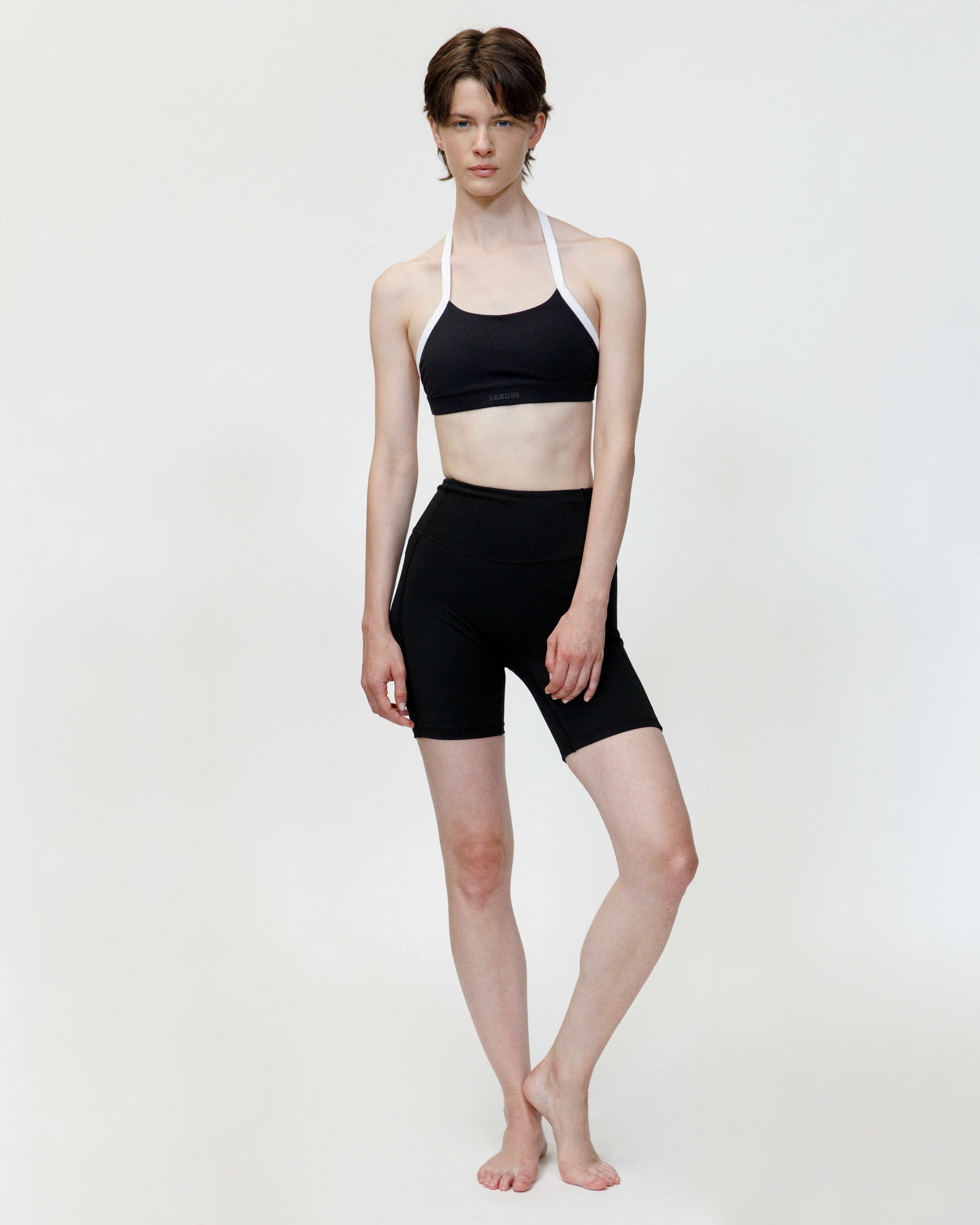 Person wearing a black sports bra and black shorts on a white background