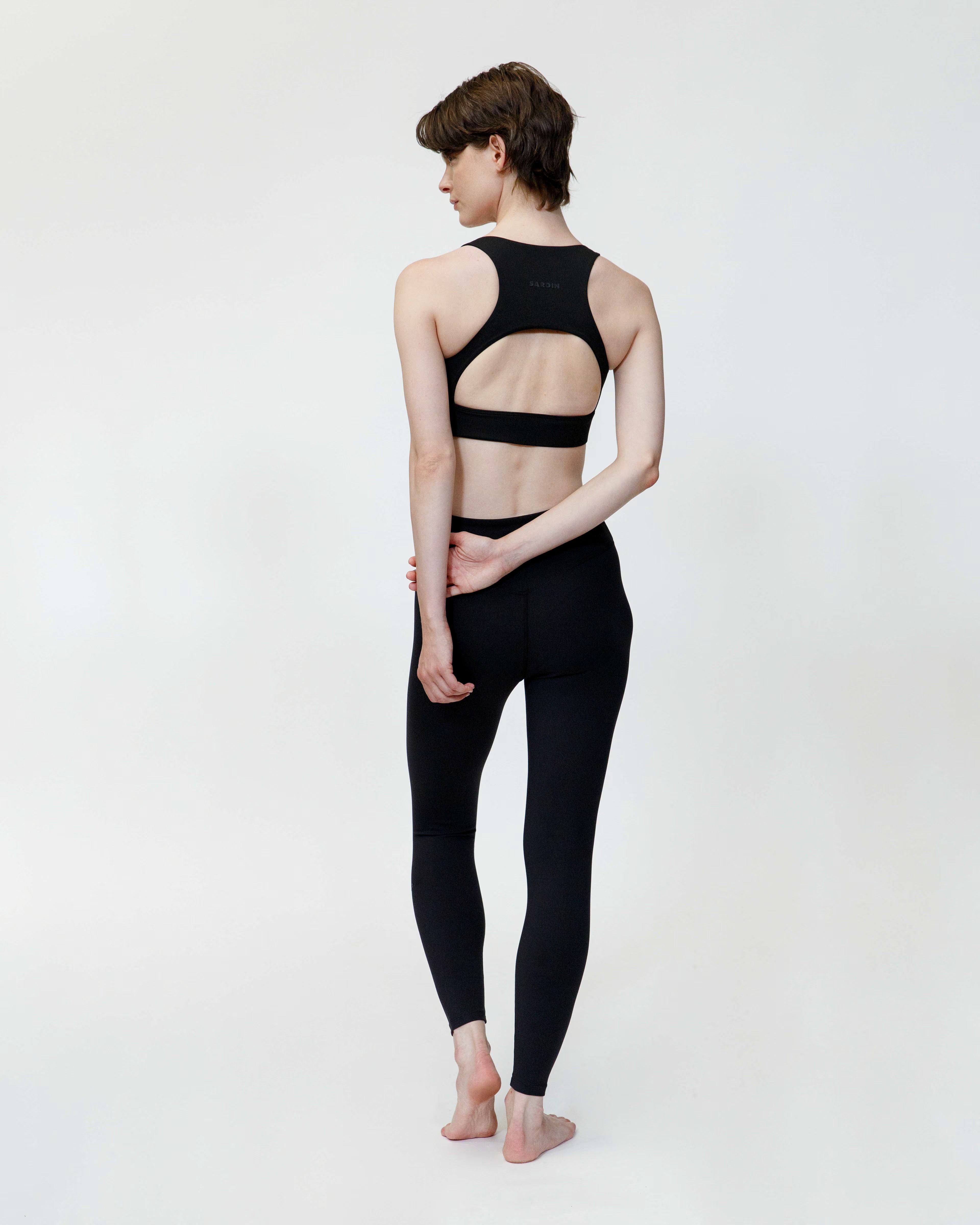 Person wearing a black open-back top and leggings on a white background