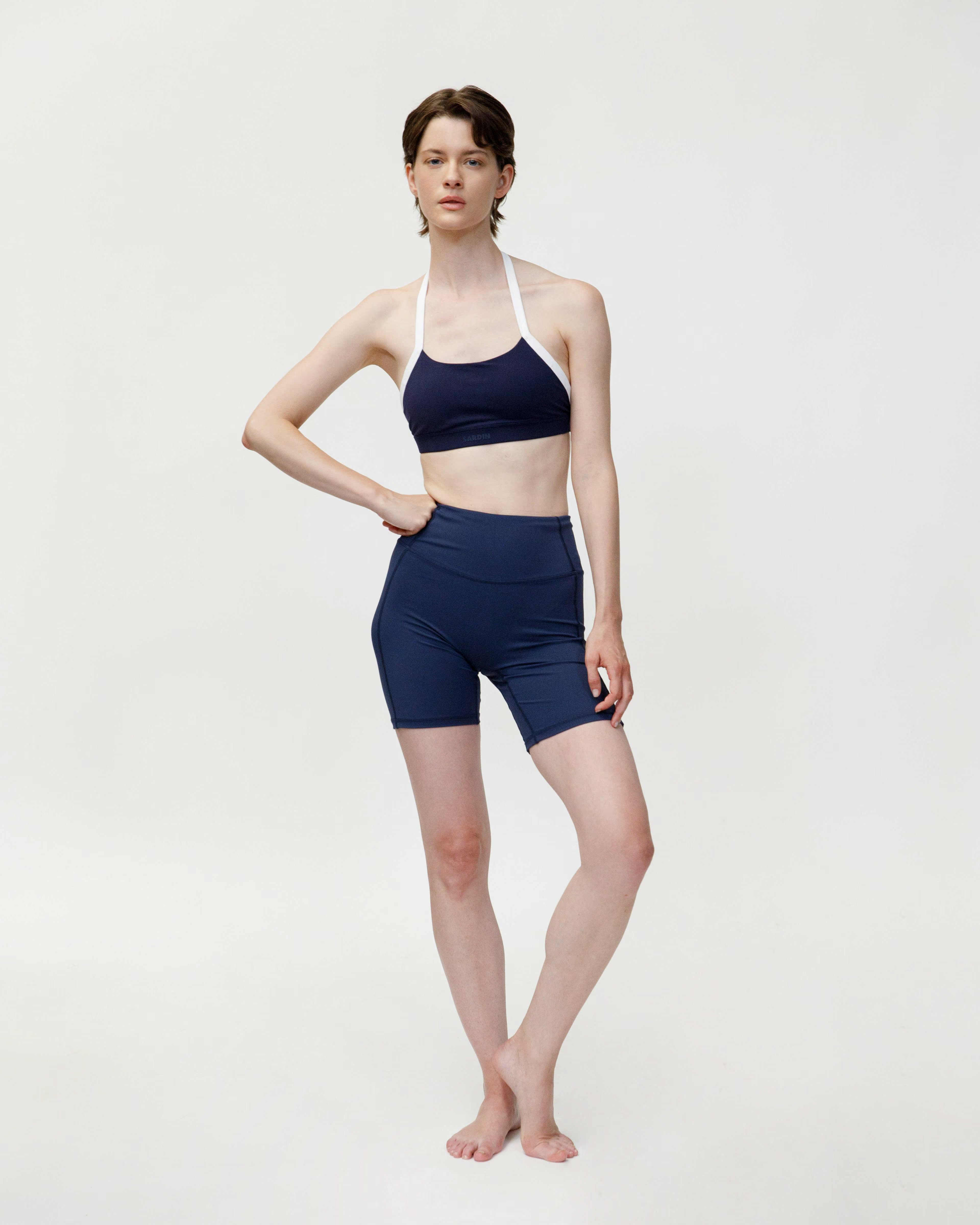 Woman wearing a navy blue sports bra and shorts on a white background