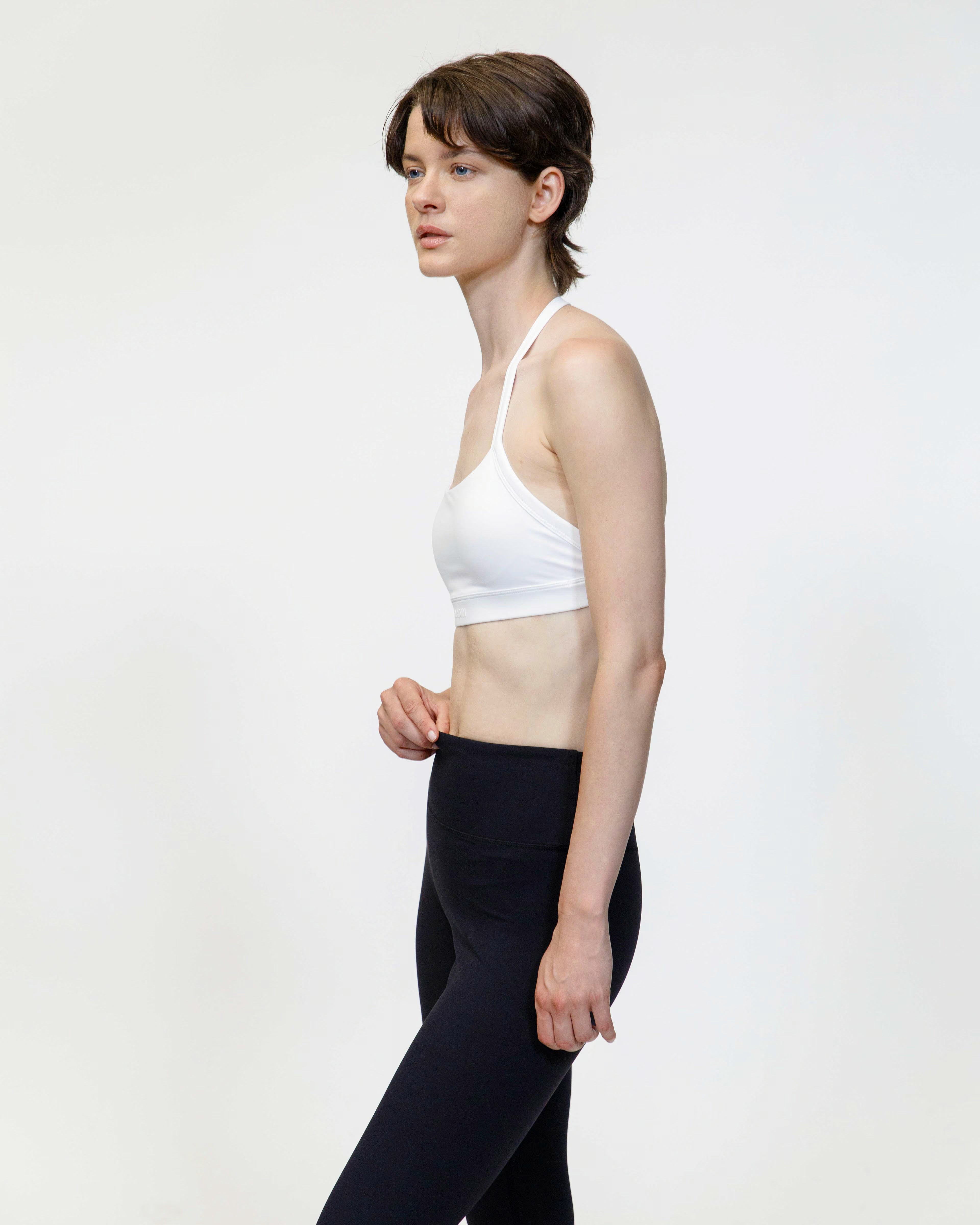 Woman wearing a white sports bra and black leggings on a plain background